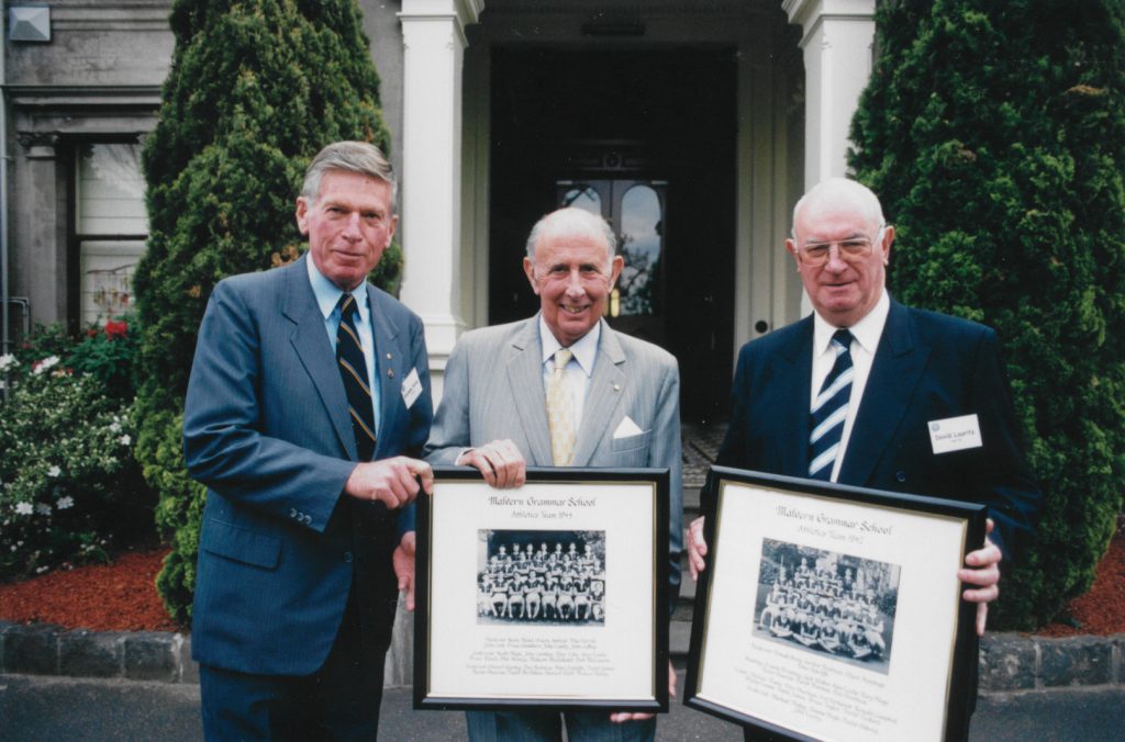 Three men holding framed pictures in front of a house.