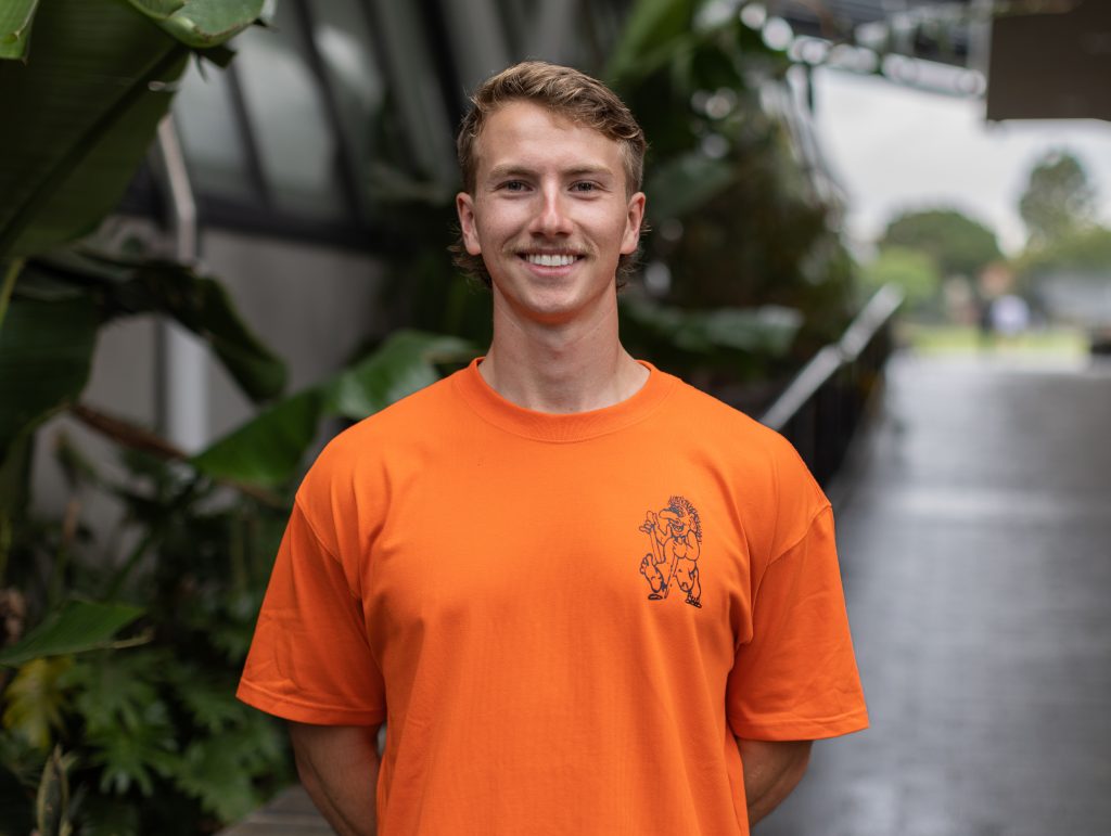 A young man in an orange t - shirt smiling.