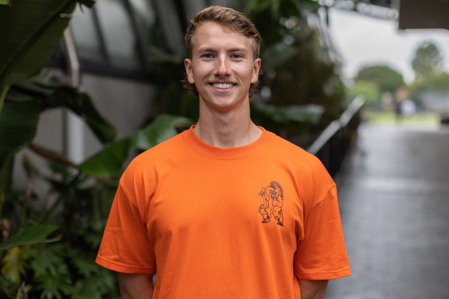 A young man in an orange t - shirt smiling.
