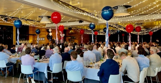 A large room full of people sitting at tables with balloons.