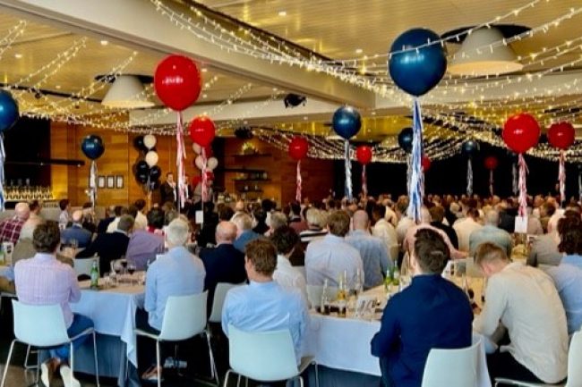 A large room full of people sitting at tables with balloons.